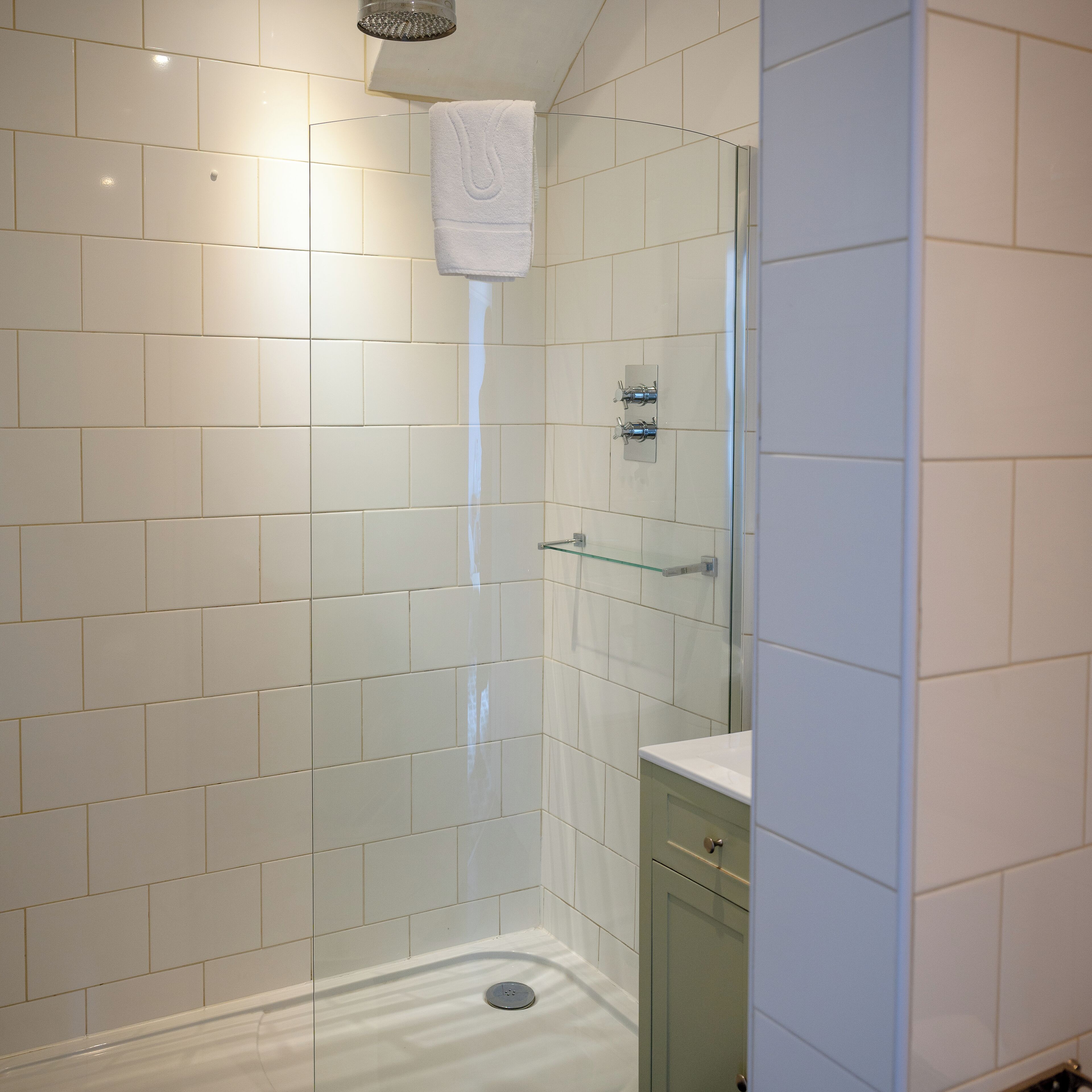 A modern bathroom with white tiles, a glass shower enclosure, and a glass shower head.