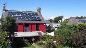 Uma casa vermelha com painéis solares no telhado e um jardim na frente.