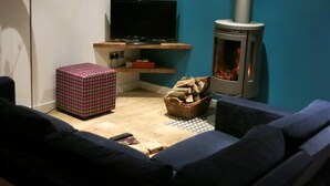 Uma sala de estar aconchegante com um sofá, uma televisão, lareira e uma mesa pequena com um cesto de lenha.
