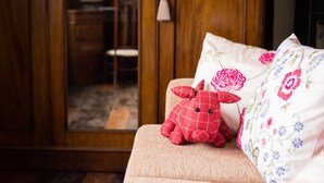 A plush toy on a sofa with floral pillows, a wooden wardrobe, and a glimpse of a dining area. - Huntlands Farm (Worcester)