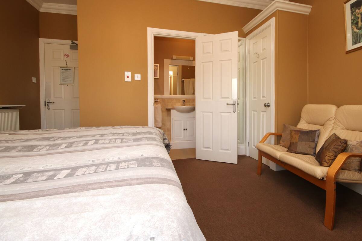 Een slaapkamer met een bed, een stoel, en een zichtbare badkamer door een geopende deur, plus een radiator.
