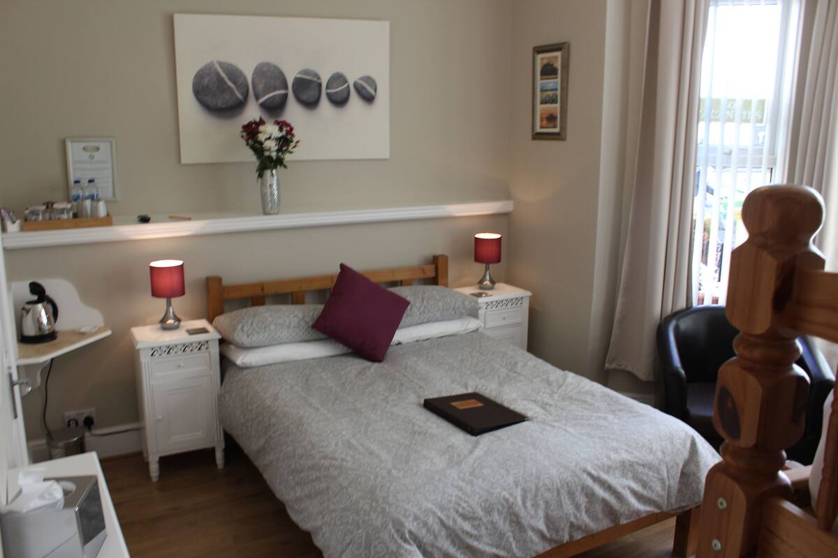 Een netjes ingerichte slaapkamer met een bed, twee nachtkastjes, een lamp, een vaas met bloemen en een kunstwerk aan de muur.