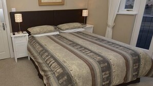 A bedroom with a large bed, two bedside tables with lamps, a window with curtains, and a door with a handle.