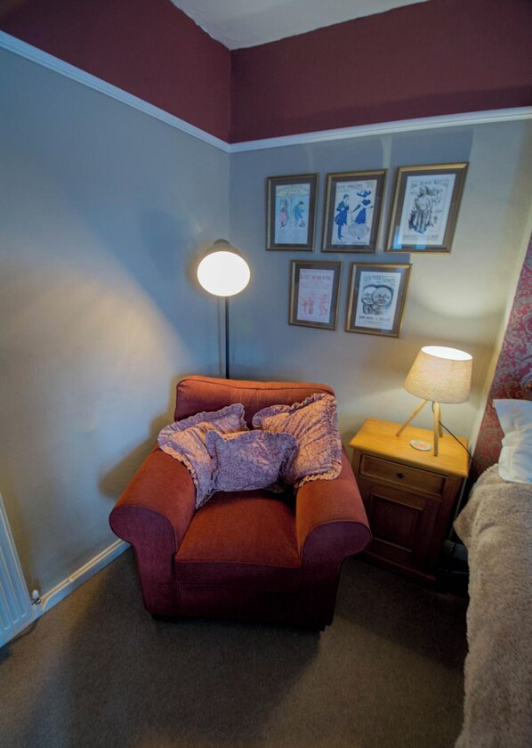 A room with a single bed, a bedside table with a lamp, a chair with a blanket, and a wall with framed pictures. - Lea House Bed and Breakfast (Ross-on-Wye)