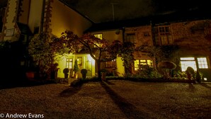 Un edificio de fachada de piedra, una entrada iluminada y un camino de acceso de grava.