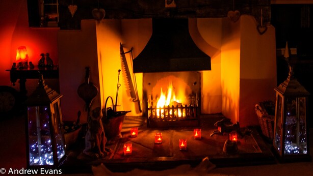 Una chimenea acogedora con fuego crepitante, rodeada de velas y objetos decorativos.