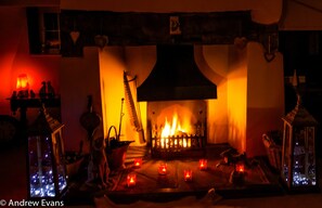 A cozy fireplace with a roaring fire, surrounded by candles and decorative items. - Lea House Bed and Breakfast (Ross-on-Wye)