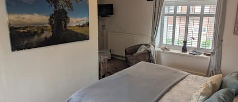A bedroom with a bed, a chair, a window with curtains, a radiator, and a painting on the wall.