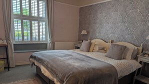 Un dormitorio con cama, ventana con cortinas, radiador y pared con estampado.