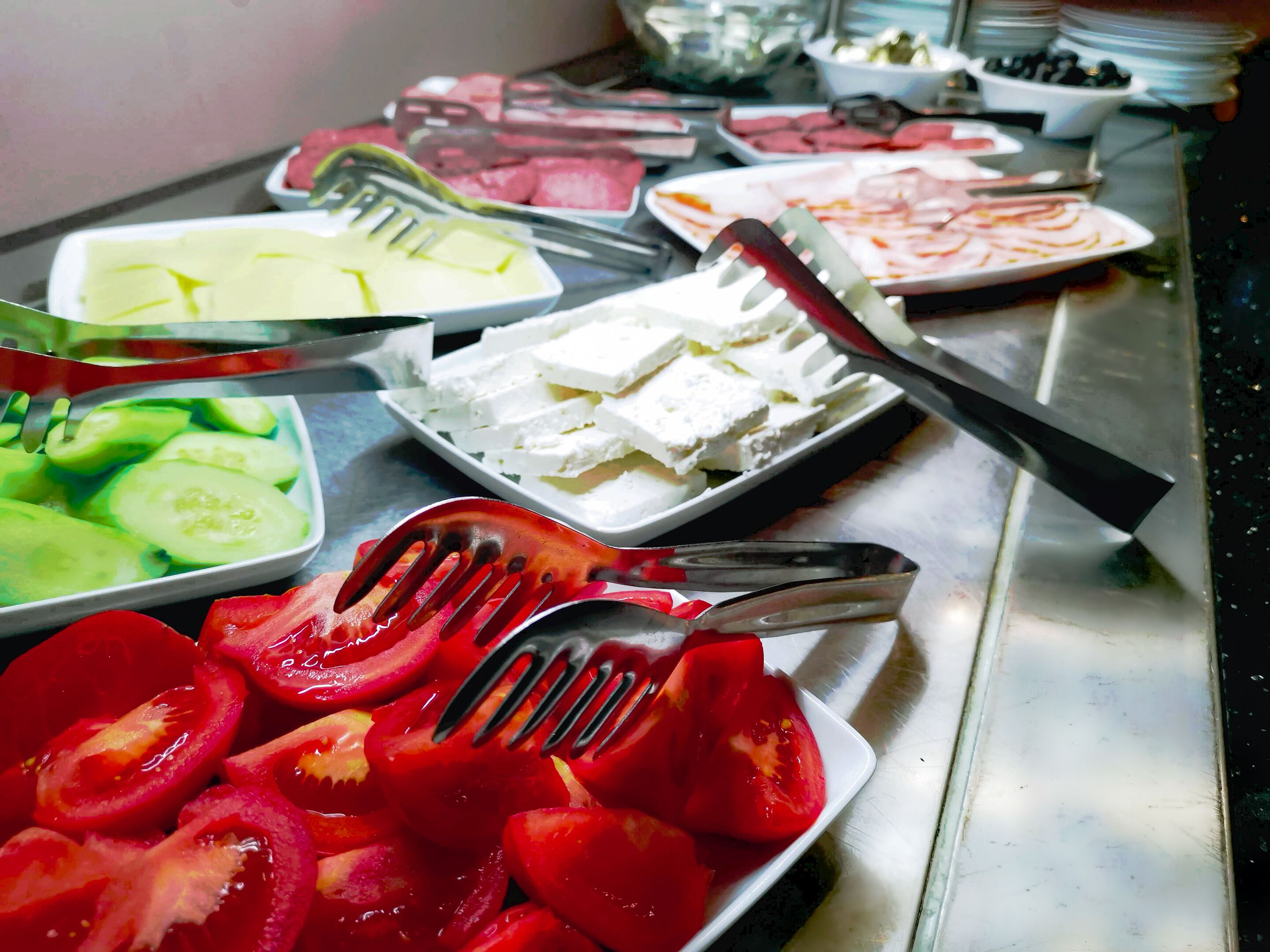 Un bufé con diversos alimentos, incluyendo pepinos en rodajas, tomates y queso.