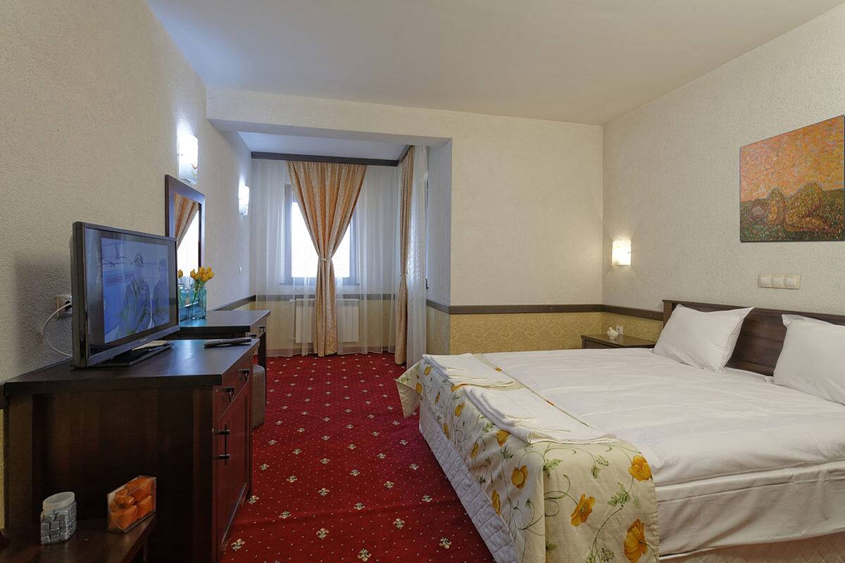 A hotel room with a bed, a television, a desk, and a window with curtains.