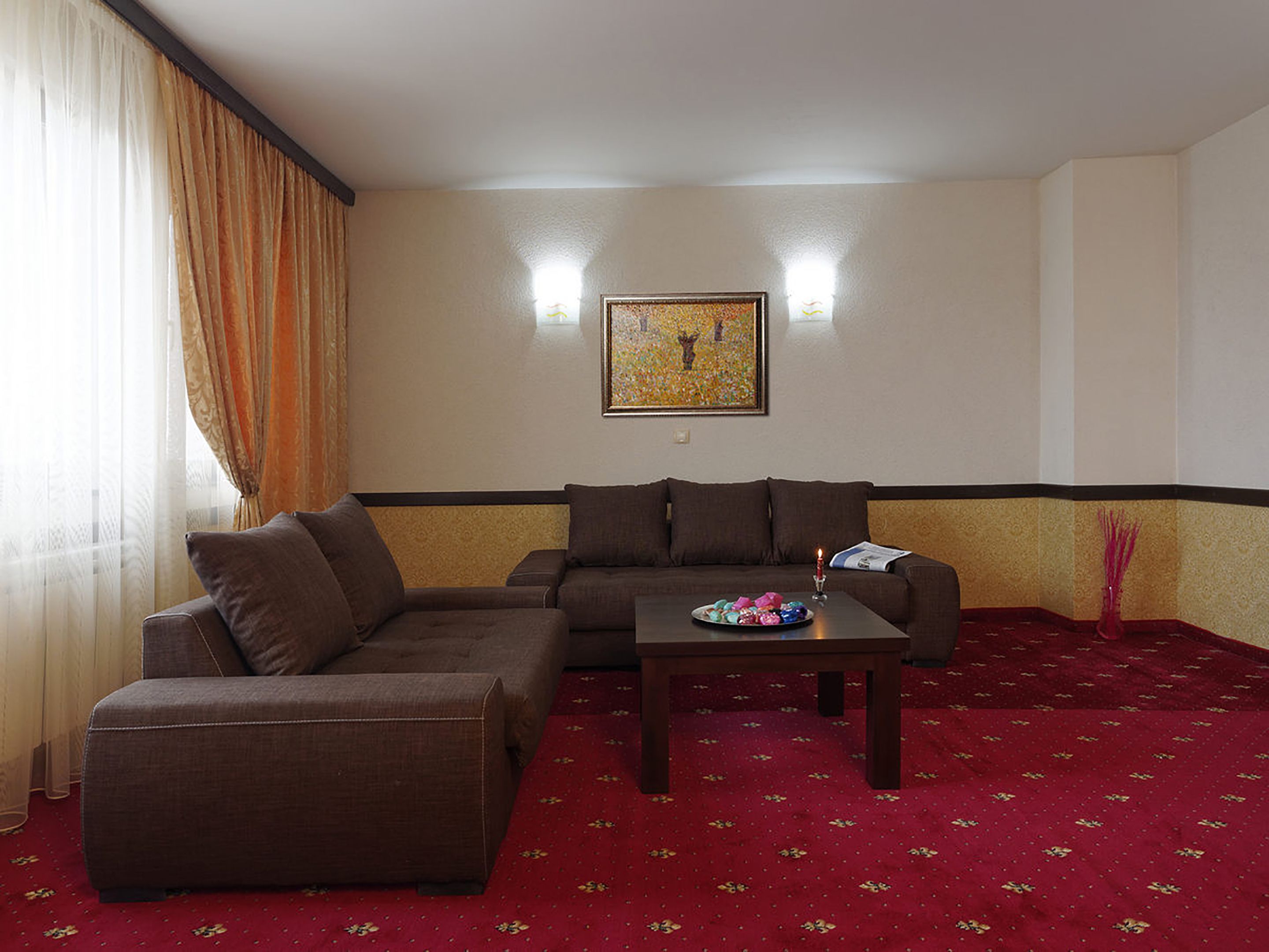 Ein Wohnzimmer mit einem braunen Sofa, einem passenden Sessel, einem Couchtisch und einem roten Teppich mit Muster.