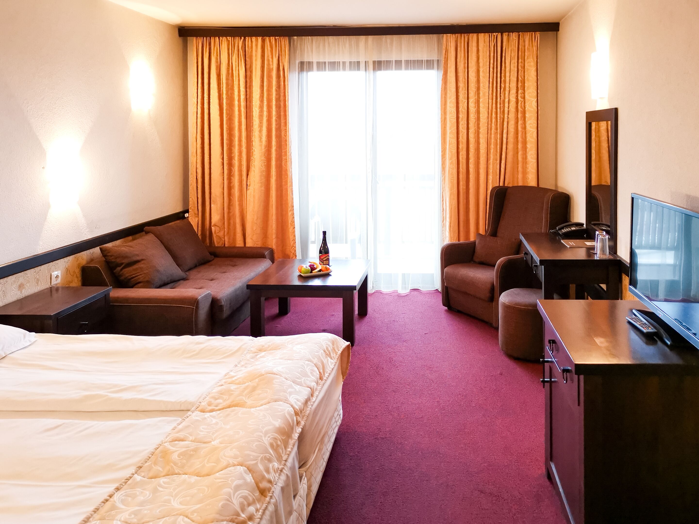 Habitació d'hotel amb llit, sofà, escriptori amb cadira, televisió i finestra amb cortines.