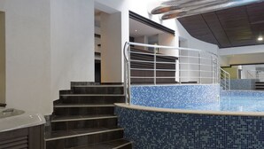 A modern indoor pool area with a tiled blue border, dark wooden steps, and a metal staircase railing. - Trinity Residence Bansko (Bansko)