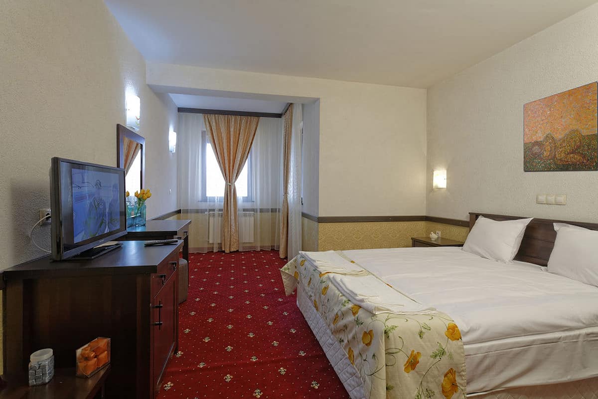A hotel room with a bed, a television, a desk, and a window with curtains.