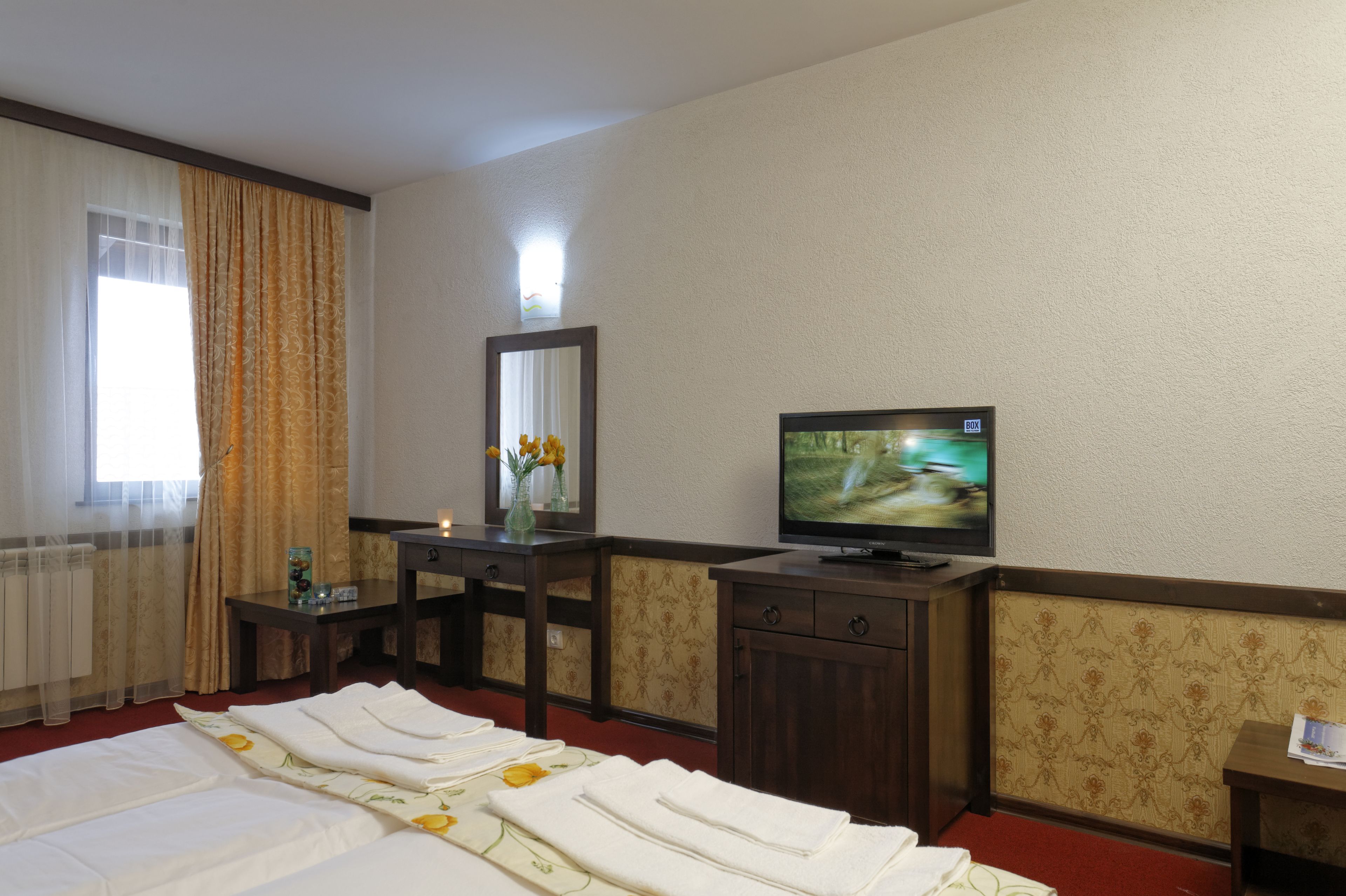 Una habitación de hotel con cama, televisión, escritorio con espejo y ventana con cortinas.