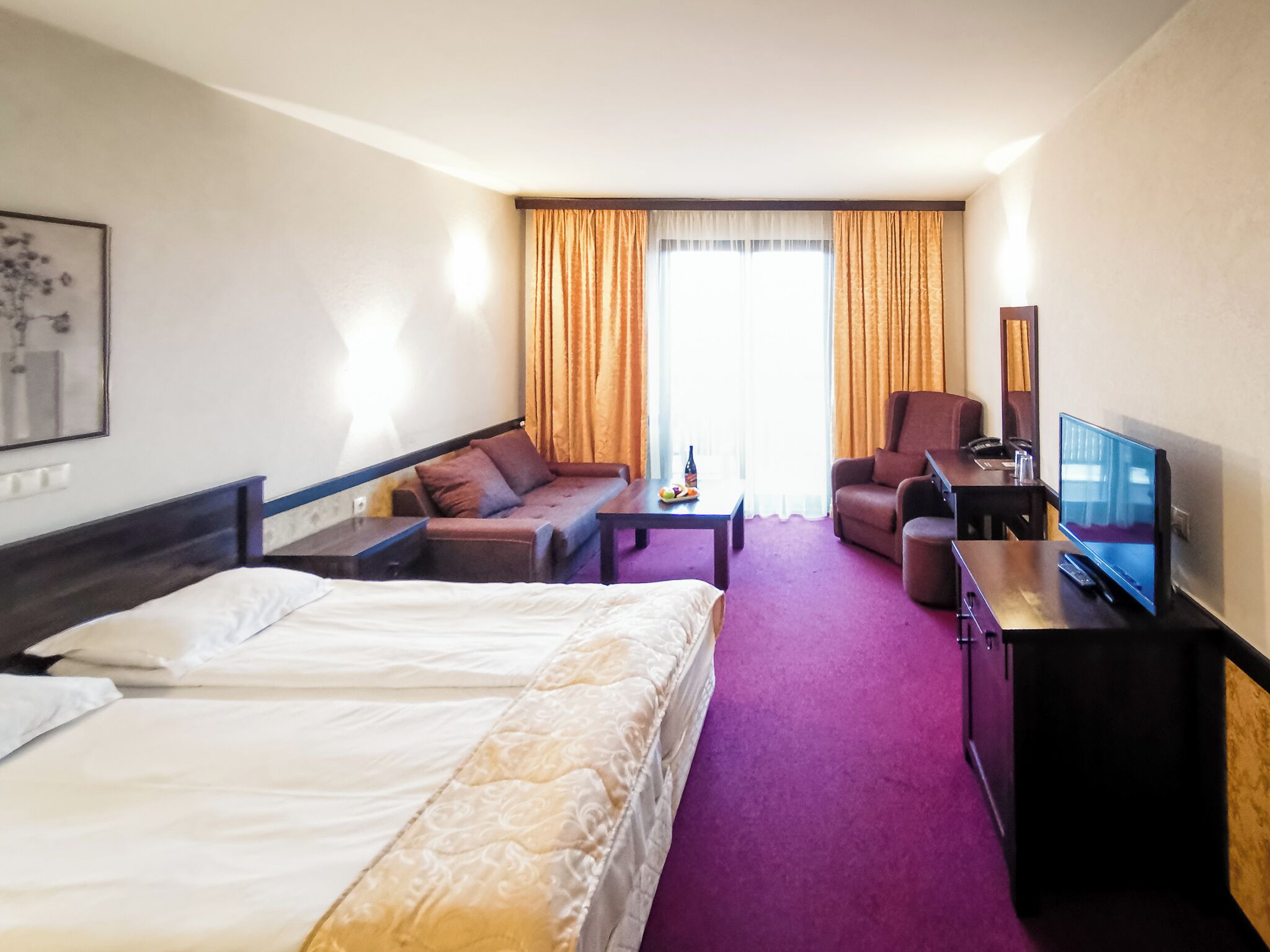 A hotel room with a bed, a sofa, a desk with a TV, and a chair.