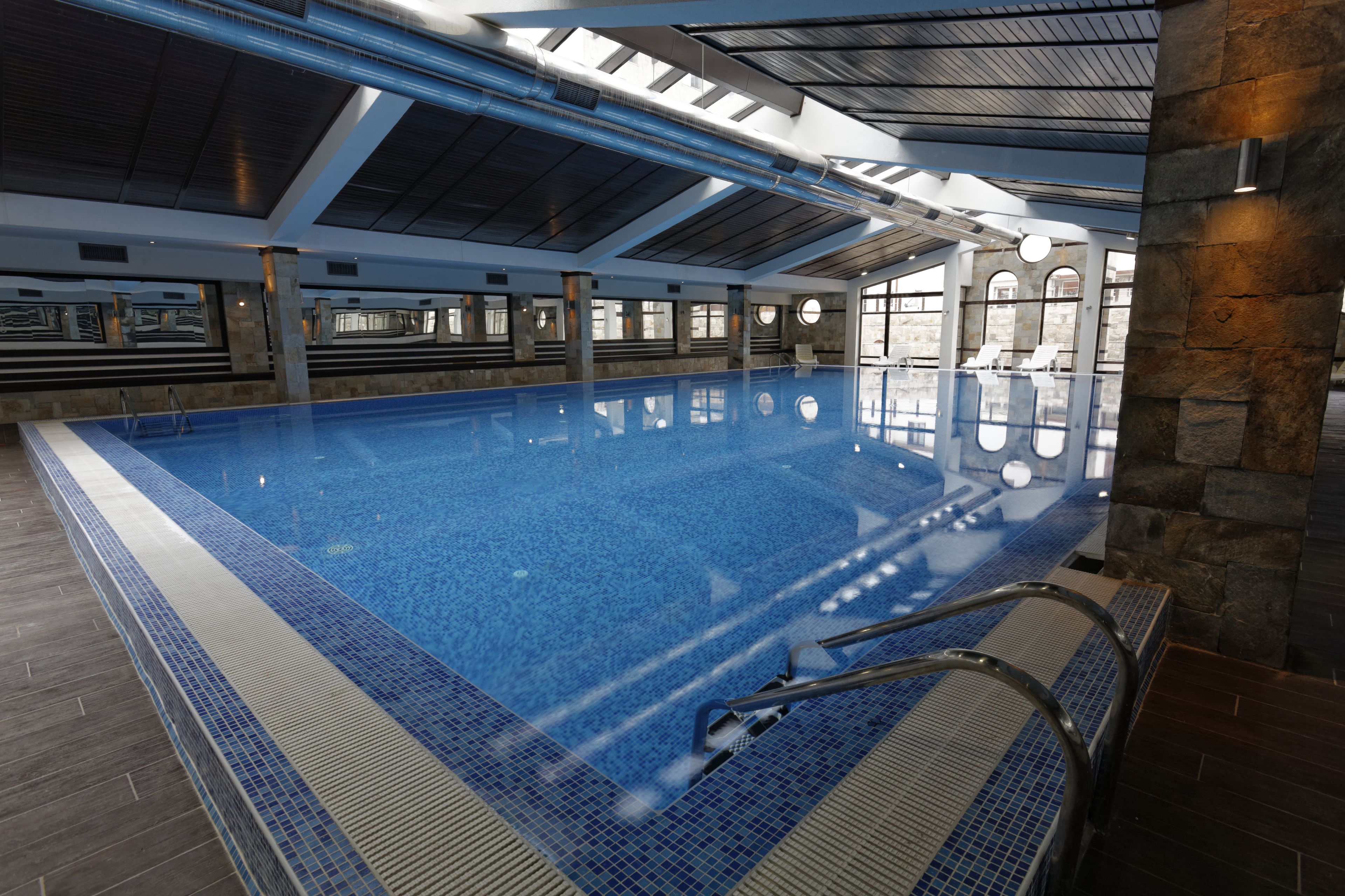 An indoor swimming pool with clear blue water, a tiled edge, and a metal ladder leading into the pool.
