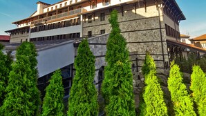 A multi-story building with balconies and stone walls, surrounded by evergreen trees. - Trinity Residence Bansko (Bansko)
