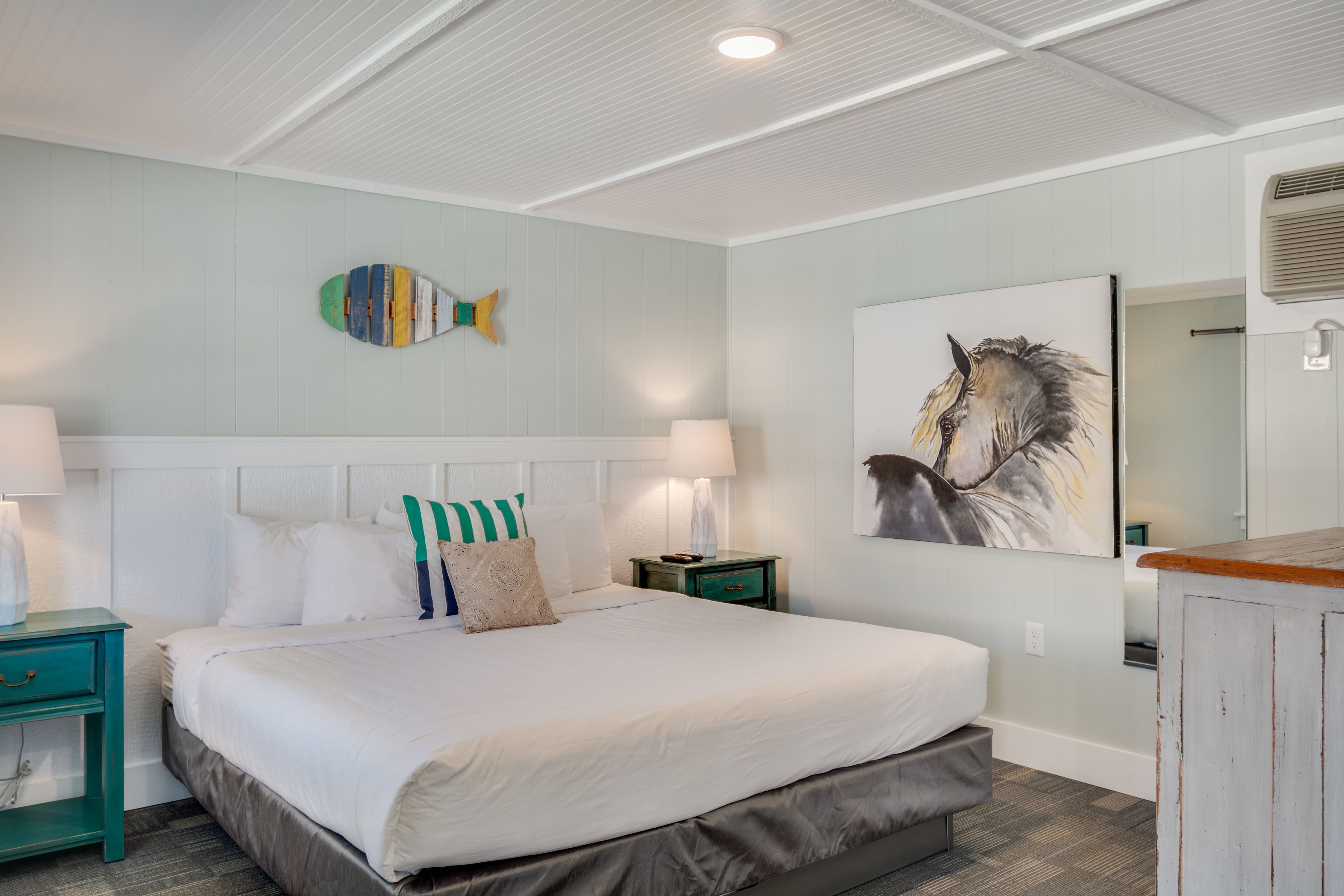 A bedroom with a large bed, two bedside tables, a wall-mounted fish decoration, and a horse painting.