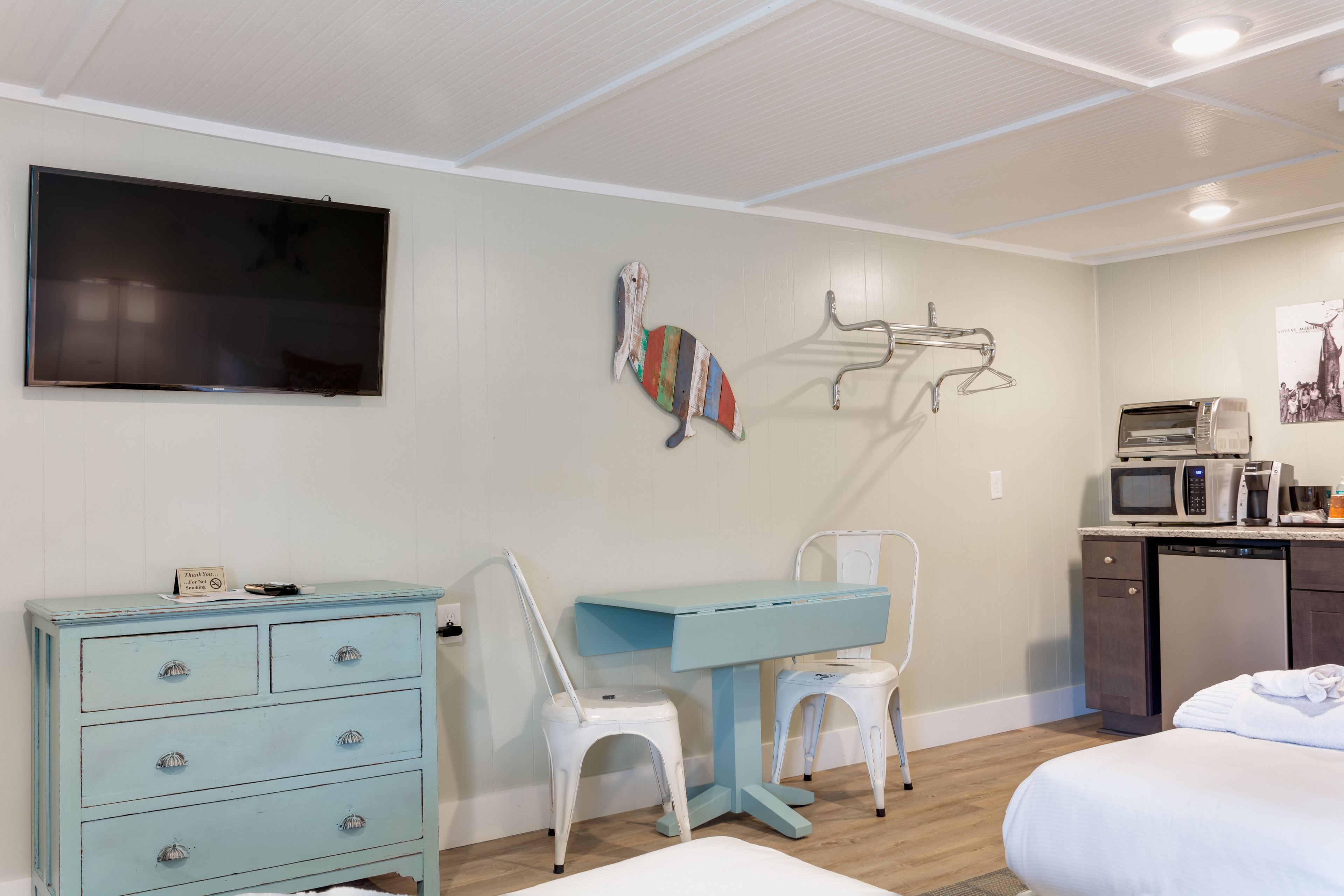 Una habitación con cama, escritorio, silla, cómoda, televisor, microondas y lavavajillas.