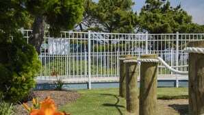 A fenced outdoor area with a grassy lawn, trees, and a wooden post with a rope. - Tar Heel Motel (Nags Head)