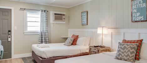 A hotel room with two beds, a window with curtains, an air conditioning unit, and a motivational sign on the wall.