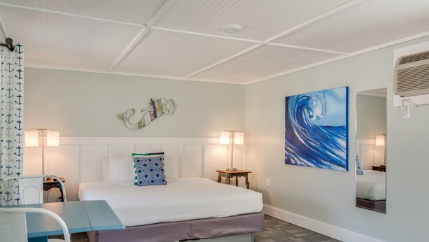 A hotel room with a bed, bedside table, lamp, and a painting on the wall. - Tar Heel Motel (Nags Head)
