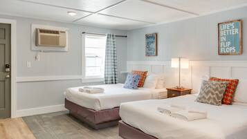 A hotel room with two beds, a window with a curtain, an air conditioning unit, a bedside table with a lamp, and a wall sign.