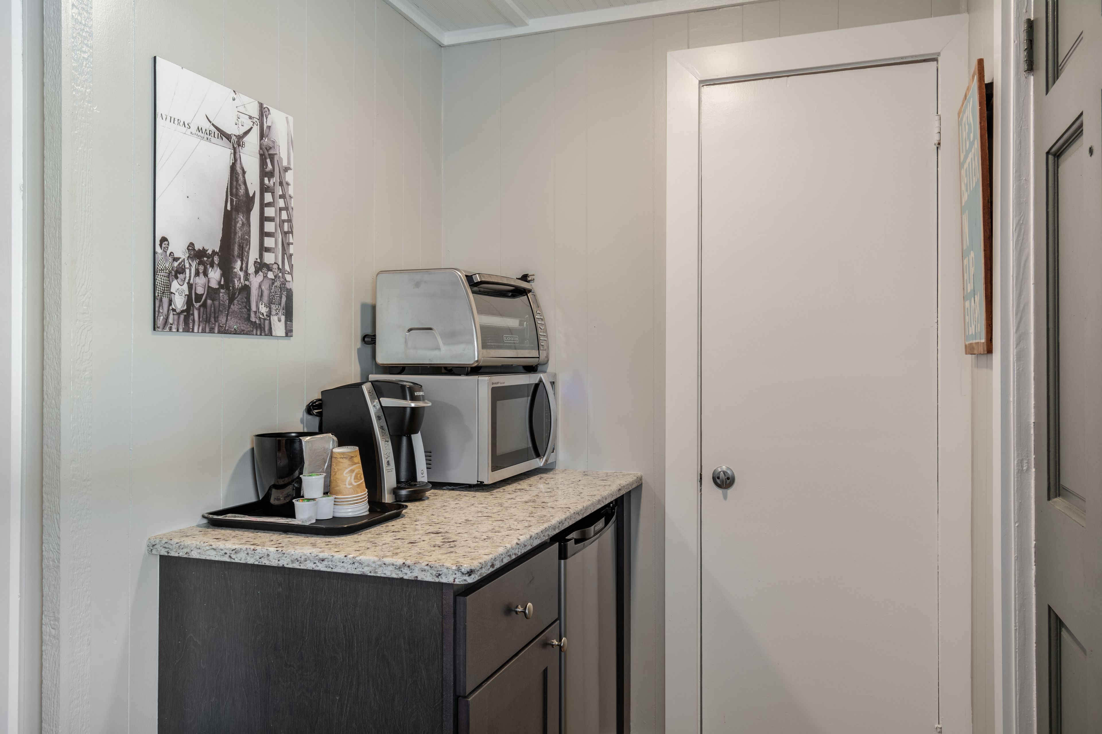 Una pequeña kitchenette con cafetera, microondas y una bandeja con tazas y jarra de café.