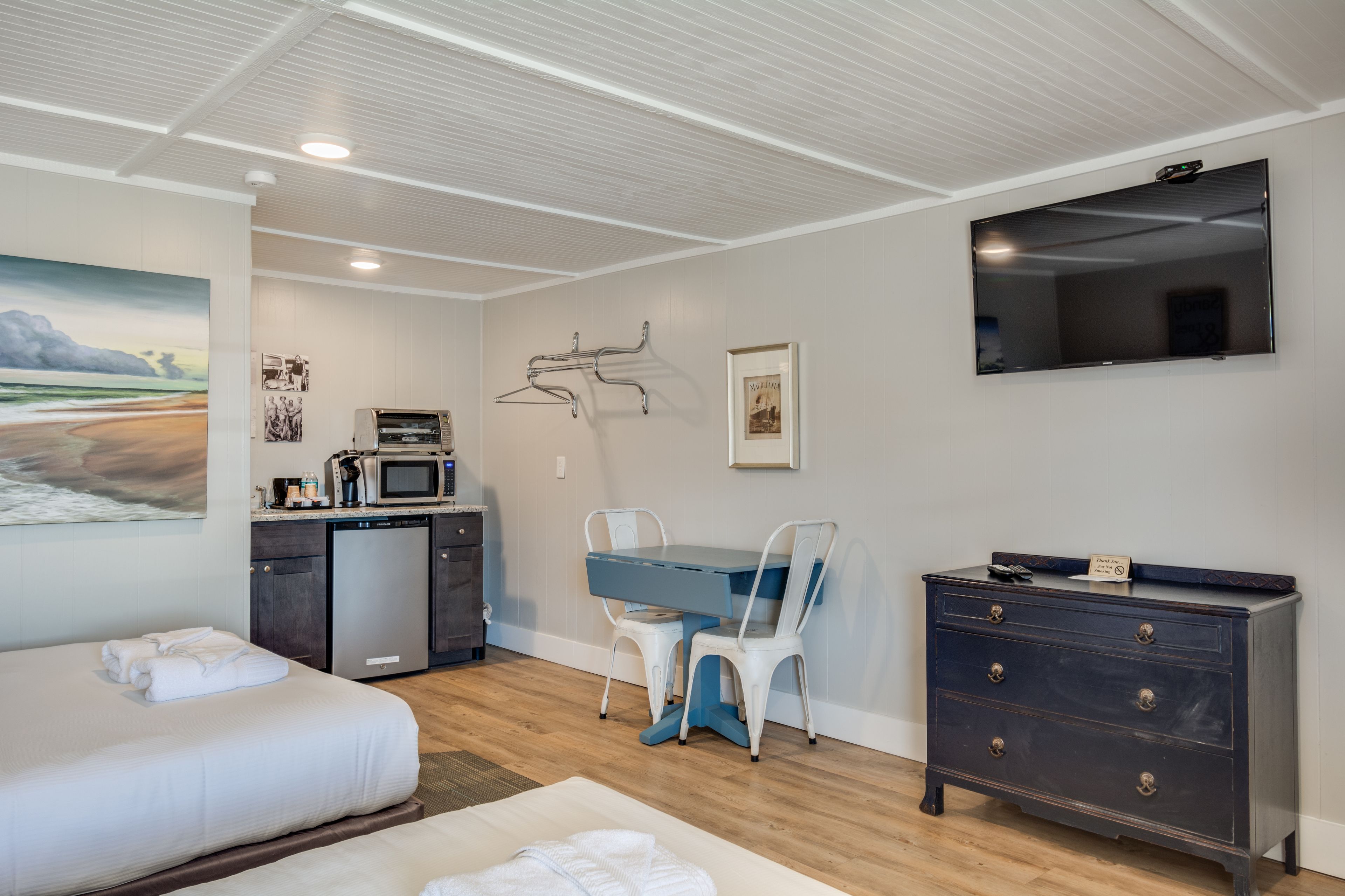 A hotel room with a bed, a desk with chairs, a dresser, a TV, a microwave, and a painting on the wall.