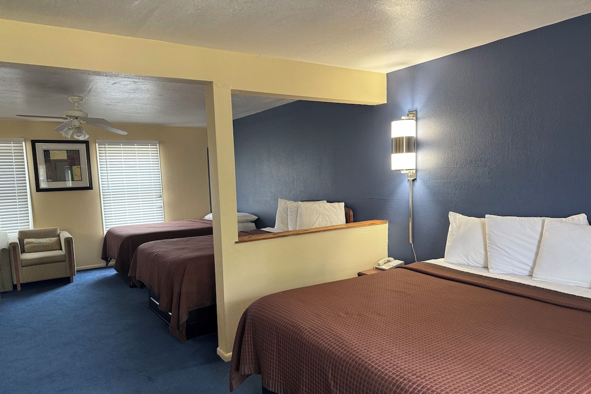 Une chambre d’hôtel avec deux lits, un bureau, une chaise, un ventilateur de plafond et une lampe de chevet.