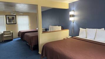 A hotel room with two beds, a desk, a chair, a ceiling fan, and a bedside lamp.
