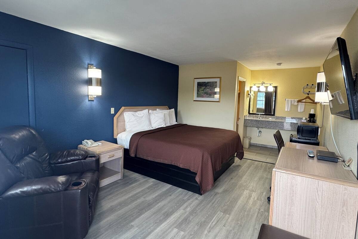 Une chambre d’hôtel comprenant un lit, un bureau, une chaise, une petite table, un miroir, un lavabo et un téléviseur.