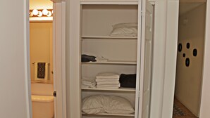 A closet with shelves containing folded towels and a bed with a white comforter. - BellaView Suites (Jersey City)