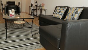 A modern living room with a black leather sofa, a glass coffee table, and a striped rug. - BellaView Suites (Jersey City)