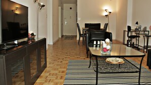 A modern living room with a flat-screen TV, a dining table with chairs, and a coffee table with decorative items. - BellaView Suites (Jersey City)