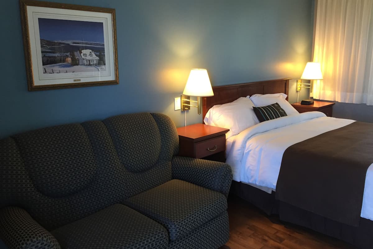 Habitación de hotel con cama, dos lámparas de noche, un cuadro en la pared y un sillón estampado.