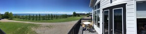 A balcony with a table and chairs, overlooking a grassy area with trees and a view of the ocean. - Hotel La Maison Blanche (New Carlisle)