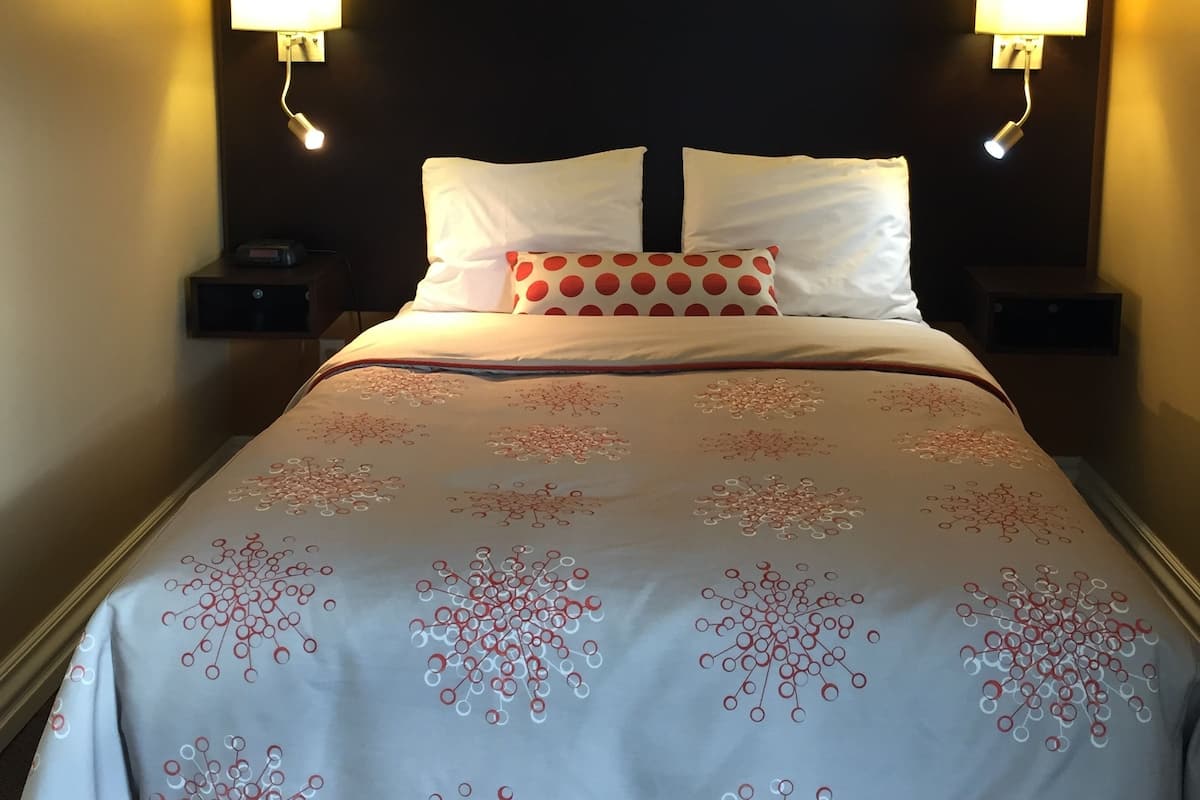 Una habitación de hotel con cama, dos mesitas de noche y dos lámparas de pared.