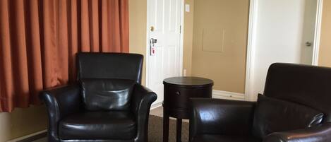 A room with two black leather chairs, a small round table, and a door with a white frame.