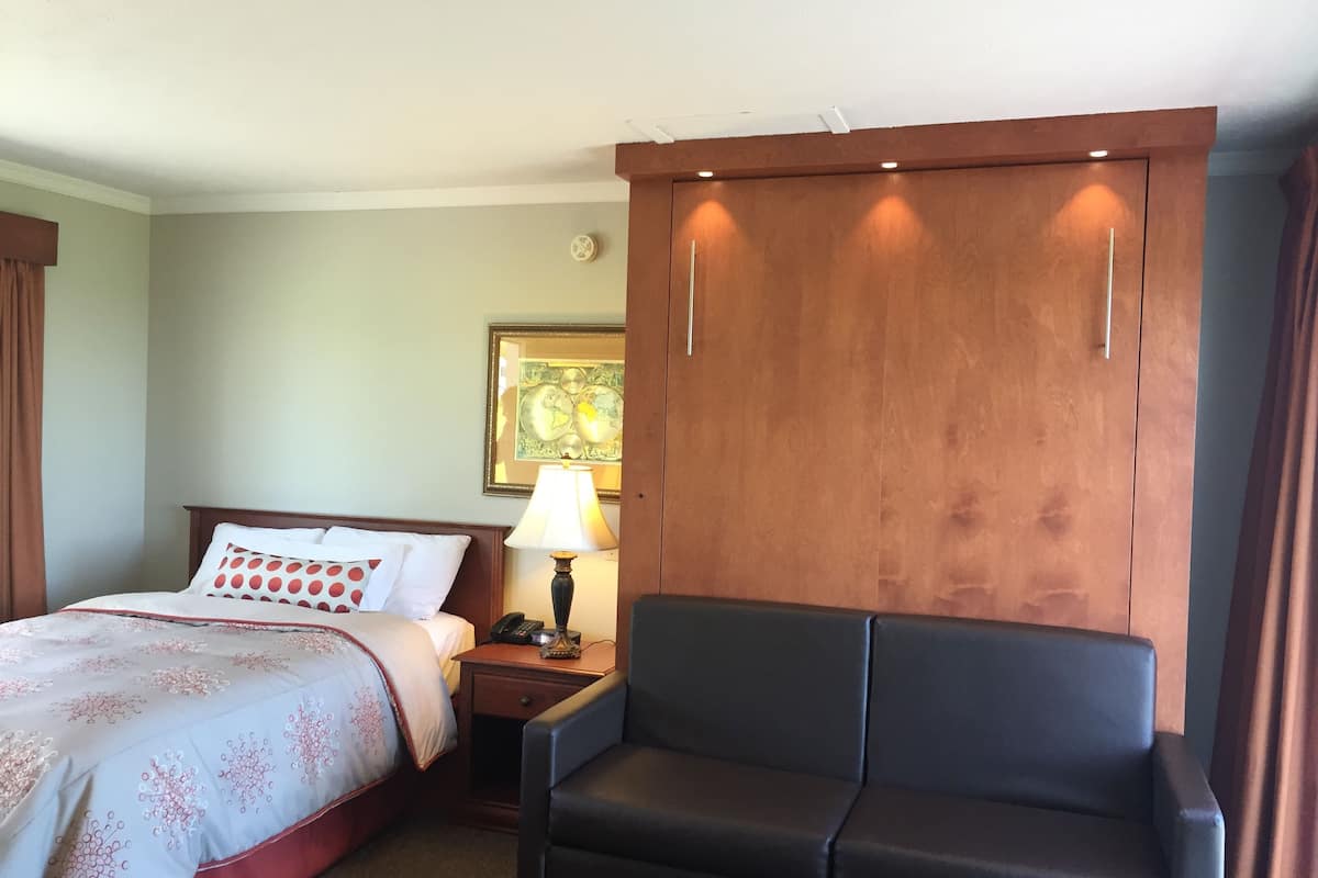 Una habitación de hotel con cama, escritorio con lámpara, silla y armario.