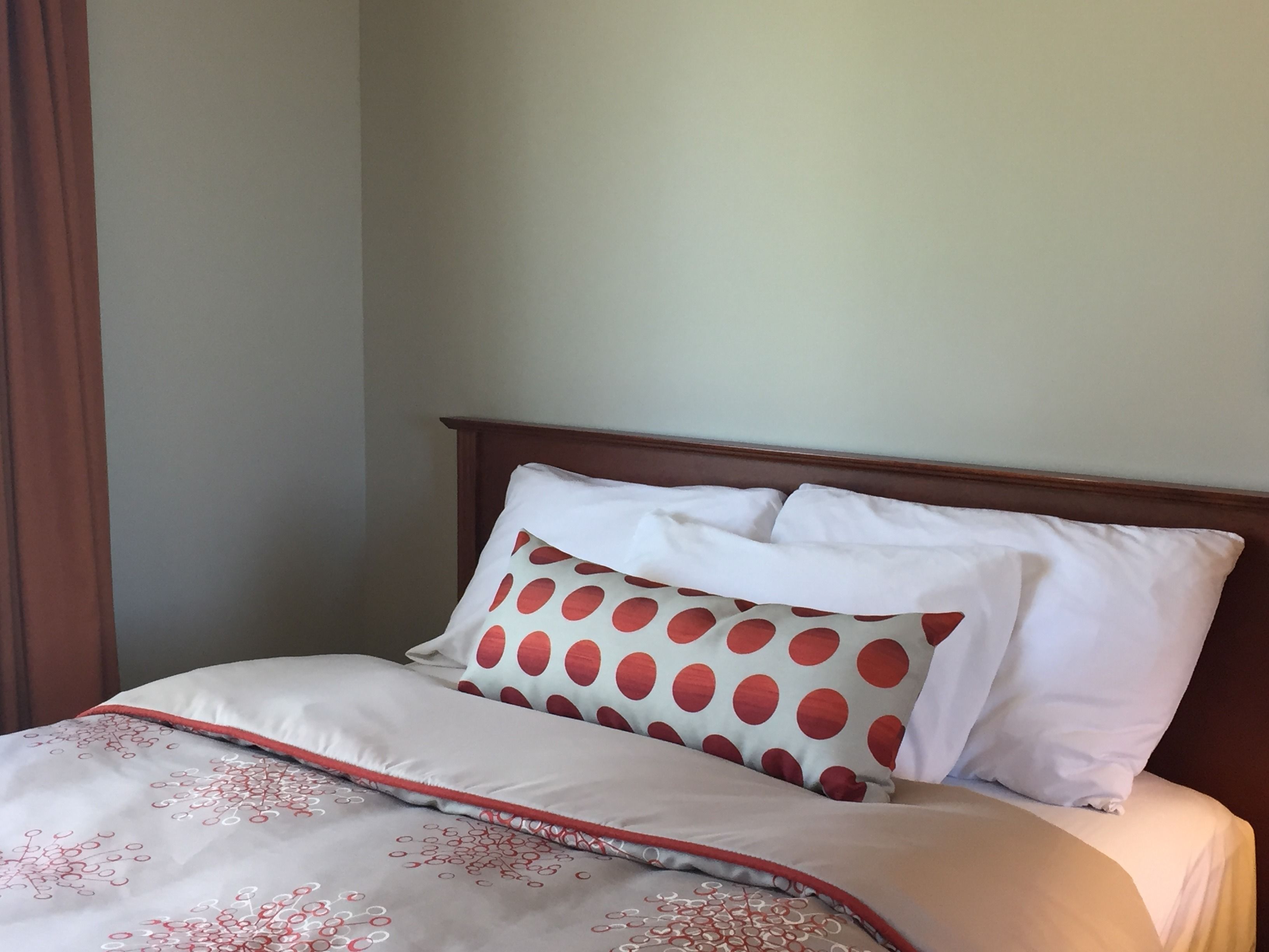 A neatly made bed with a patterned bedspread, two pillows with a polka dot design, and a wooden headboard.