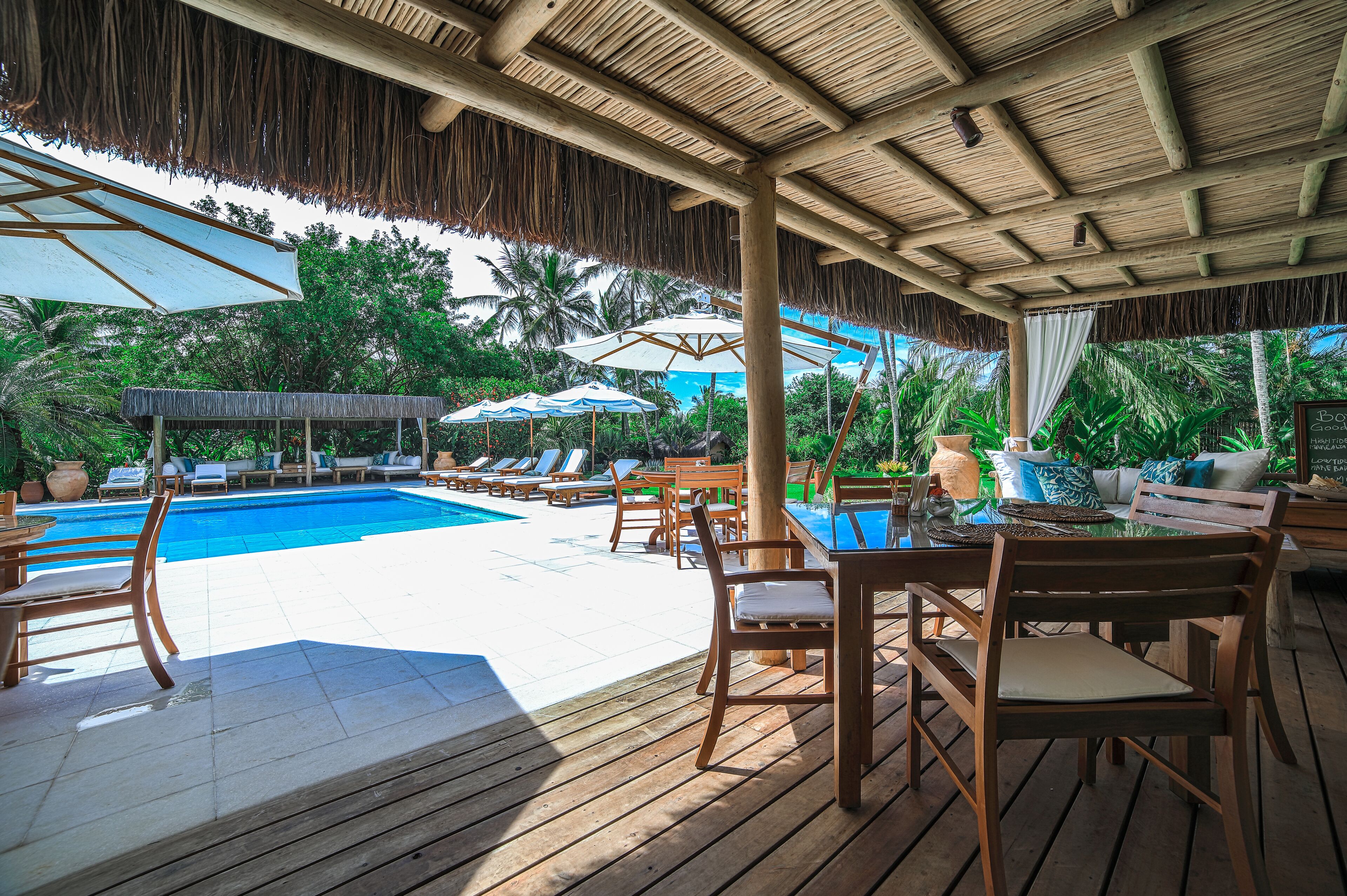 Um deck de madeira com piscina, cadeiras de sol e guarda-sóis.