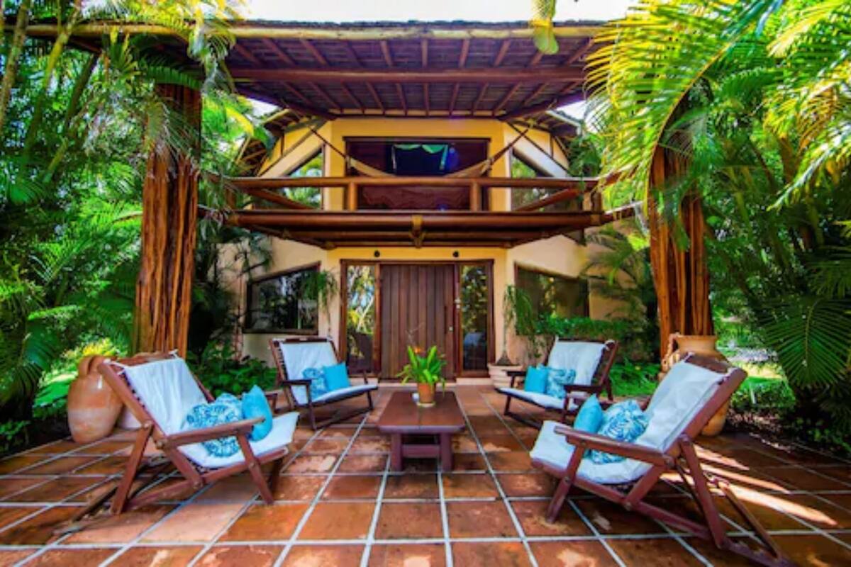 Une terrasse extérieure dotée d’une pergola en bois, d’une table centrale et de quatre fauteuils avec des coussins bleus.