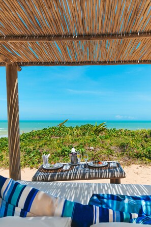 A beachside lounge with a table set for two, overlooking the ocean.