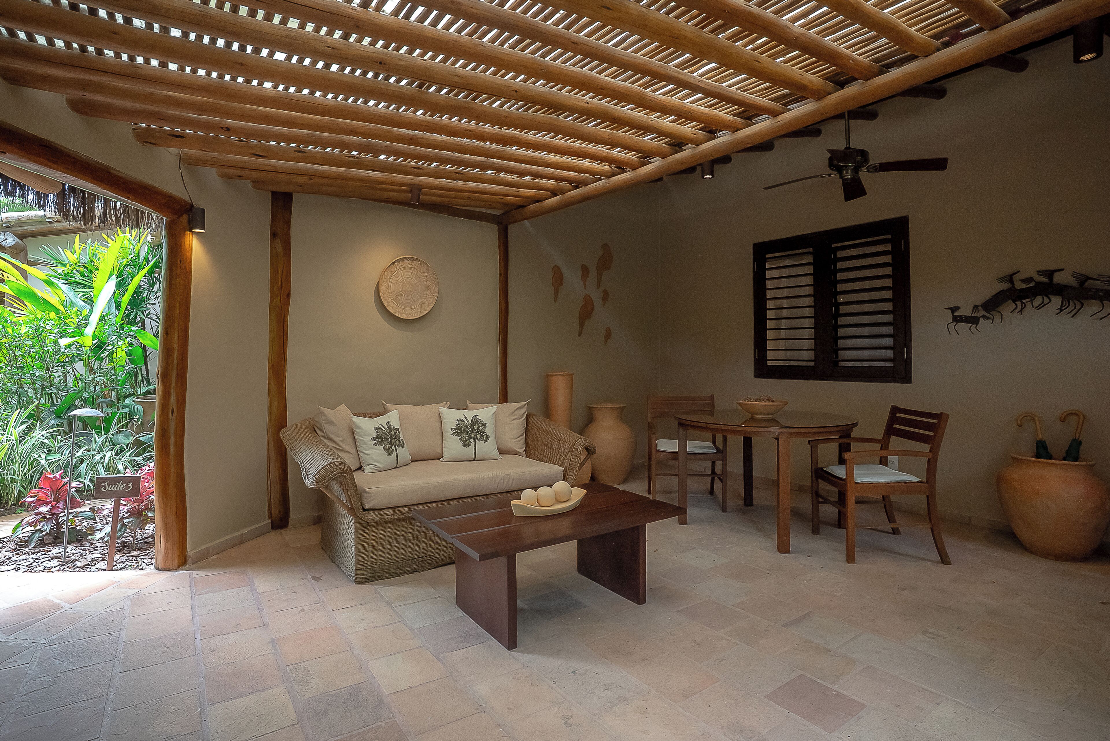 A room with a wooden ceiling, a sofa with cushions, a coffee table, a dining table with chairs, and a large vase.