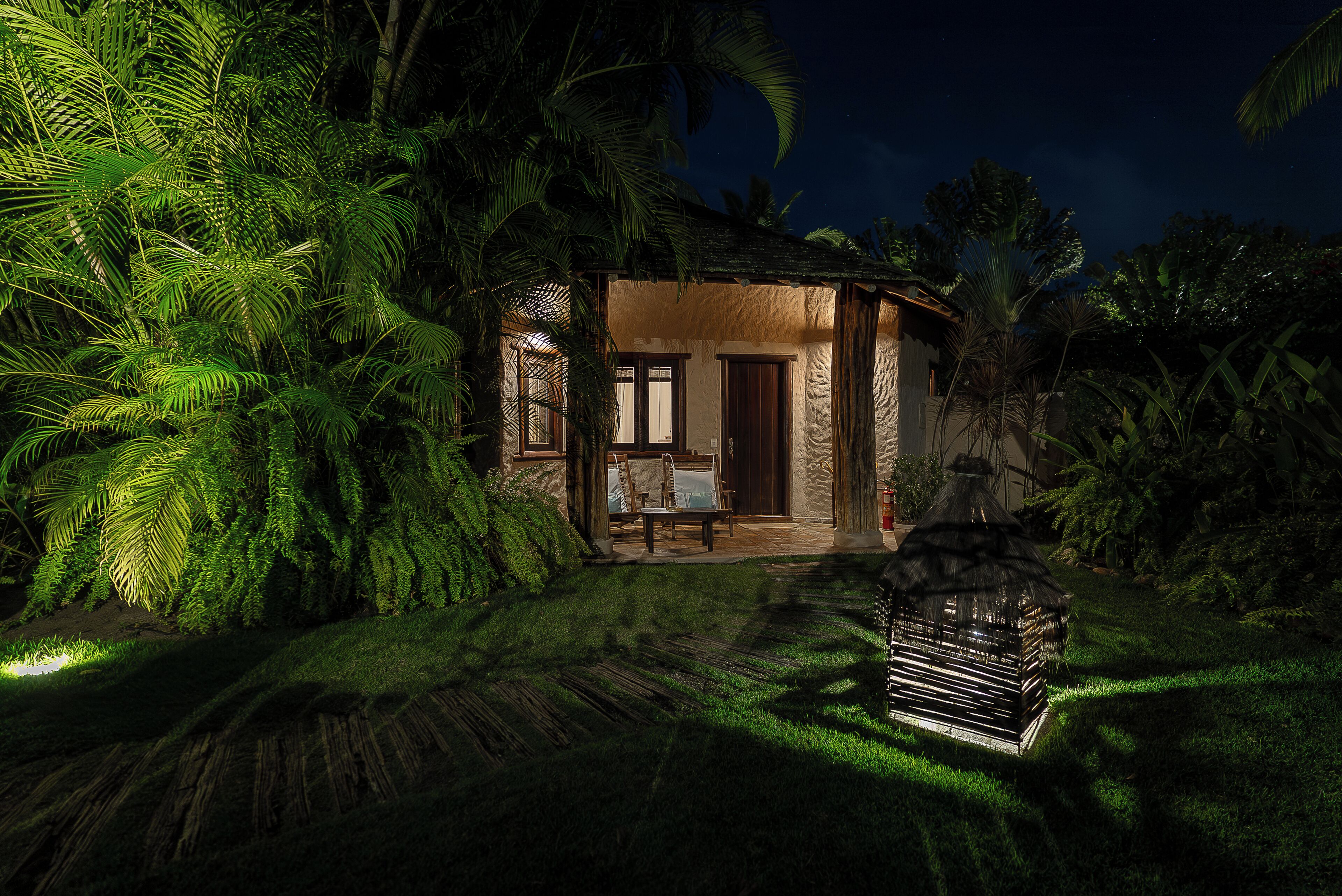 A house with a thatched roof, surrounded by dense tropical foliage.