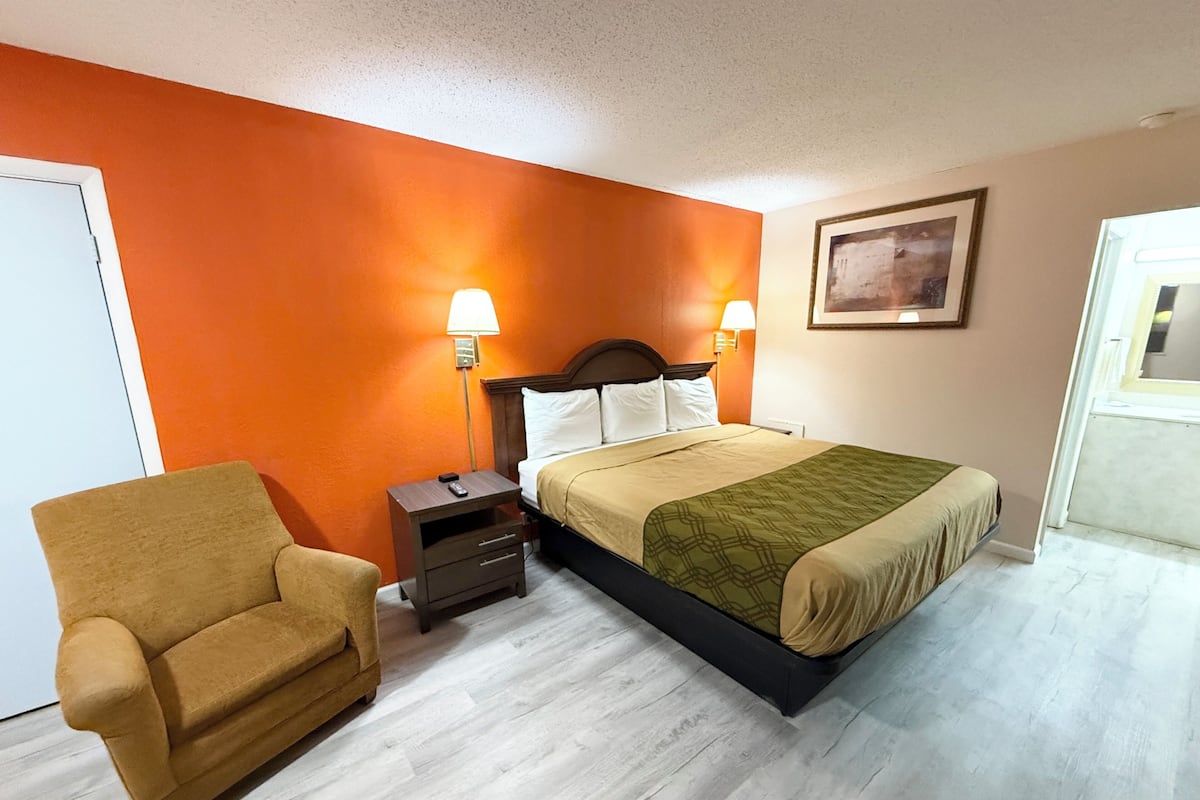 A hotel room with a bed, nightstands, a chair, and a painting on the wall.