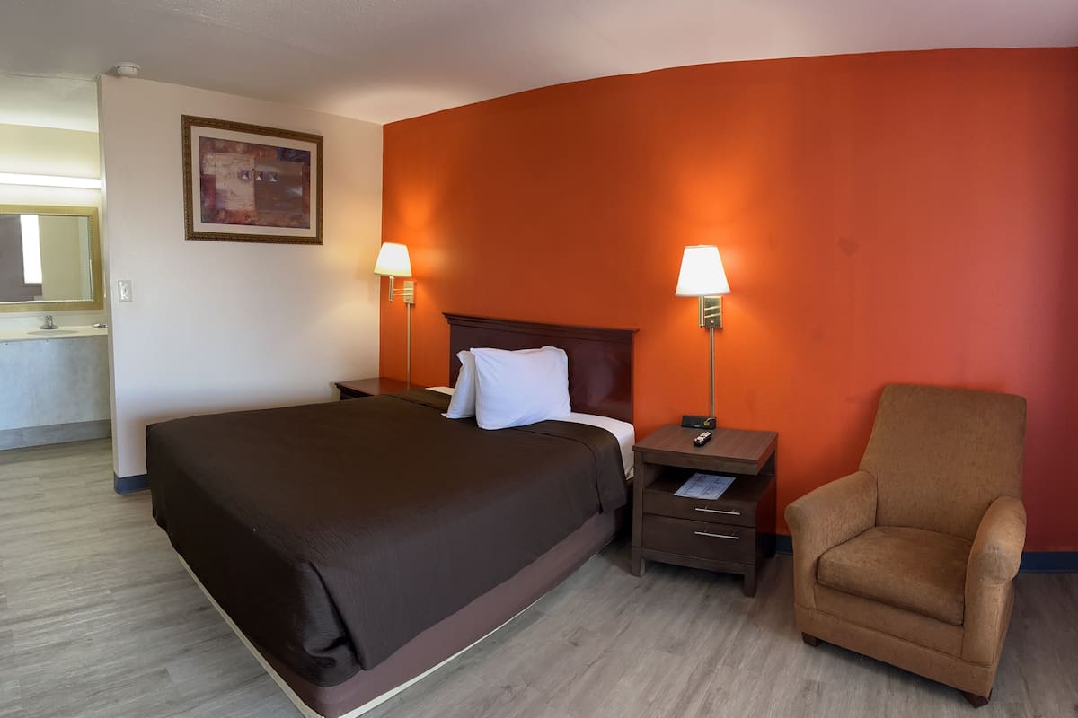 A hotel room with a large bed, two bedside lamps, a chair, and a nightstand.